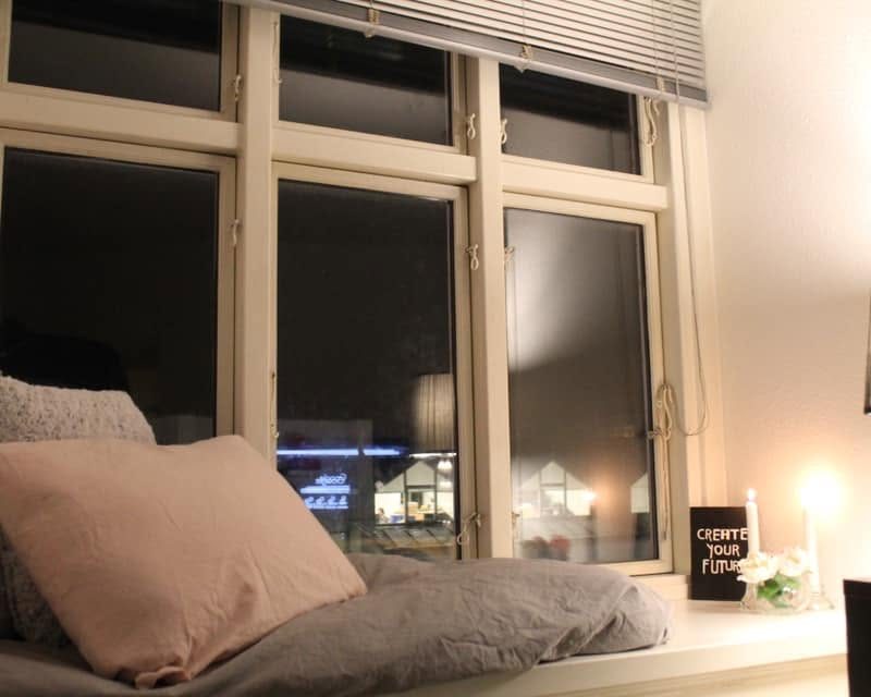 Hyggelig vindueskrog i en af boligerne med puder, dyne, tændte stearinlys og et skilt med teksten Create your future